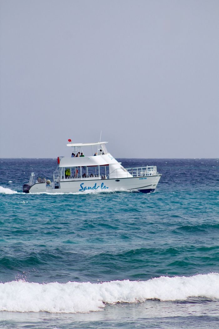 A white boat named 'Sand On' sailing across tranquil blue ocean waters on a clear day.