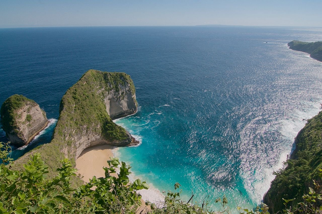 Stunning aerial view of Kelingking Beach, Bali, with turquoise waters and lush cliffs.